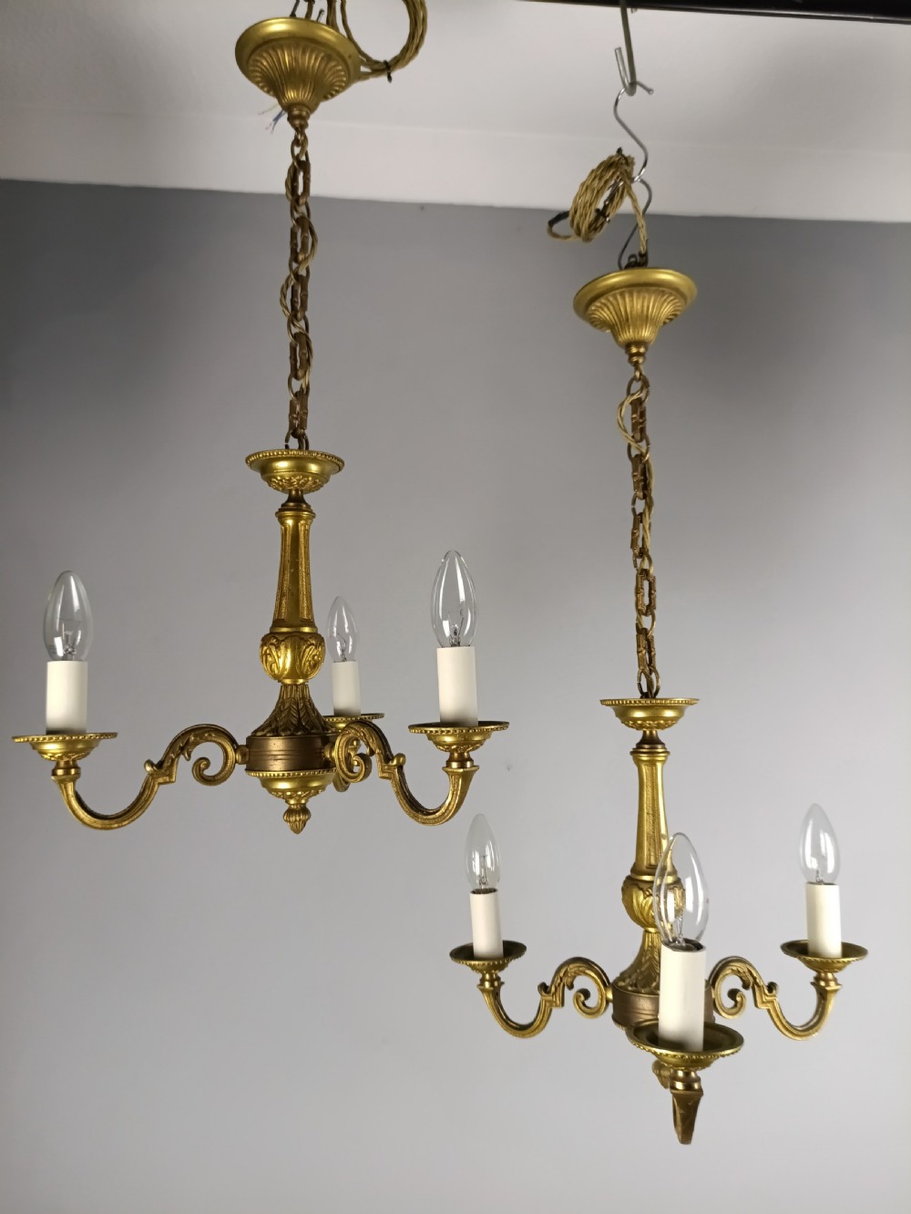 A pair of French gilt brass three-arm chandeliers featuring scrolling branches and fluted central columns suspended from metal chains. View IV