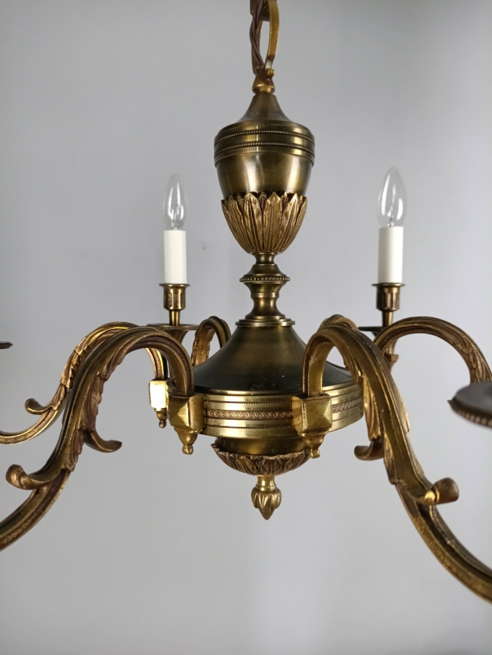 A French antique-style bronze six-arm chandelier featuring scrolling candle arms, white candle sleeves, and a central urn-shaped stem suspended from a metal chain. View II