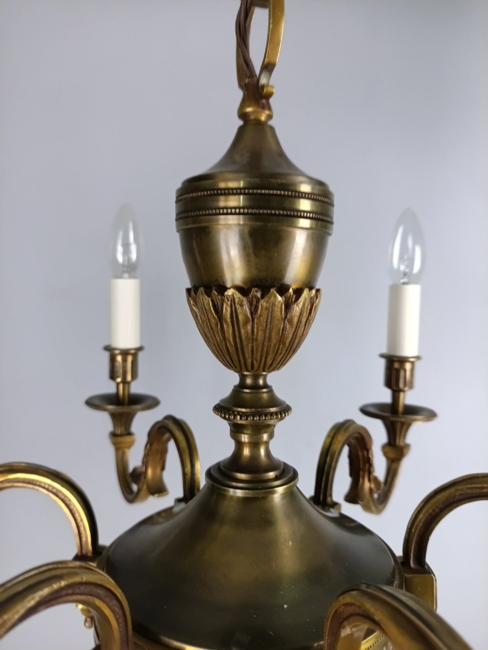 A French antique-style bronze six-arm chandelier featuring scrolling candle arms, white candle sleeves, and a central urn-shaped stem suspended from a metal chain. View IV