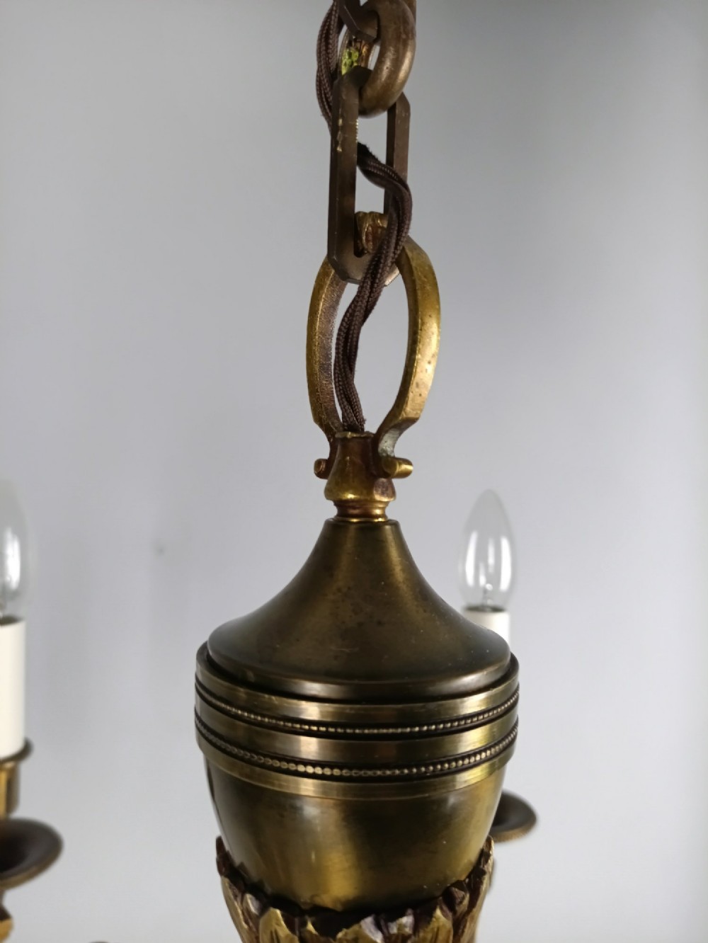 A French antique-style bronze six-arm chandelier featuring scrolling candle arms, white candle sleeves, and a central urn-shaped stem suspended from a metal chain. View V
