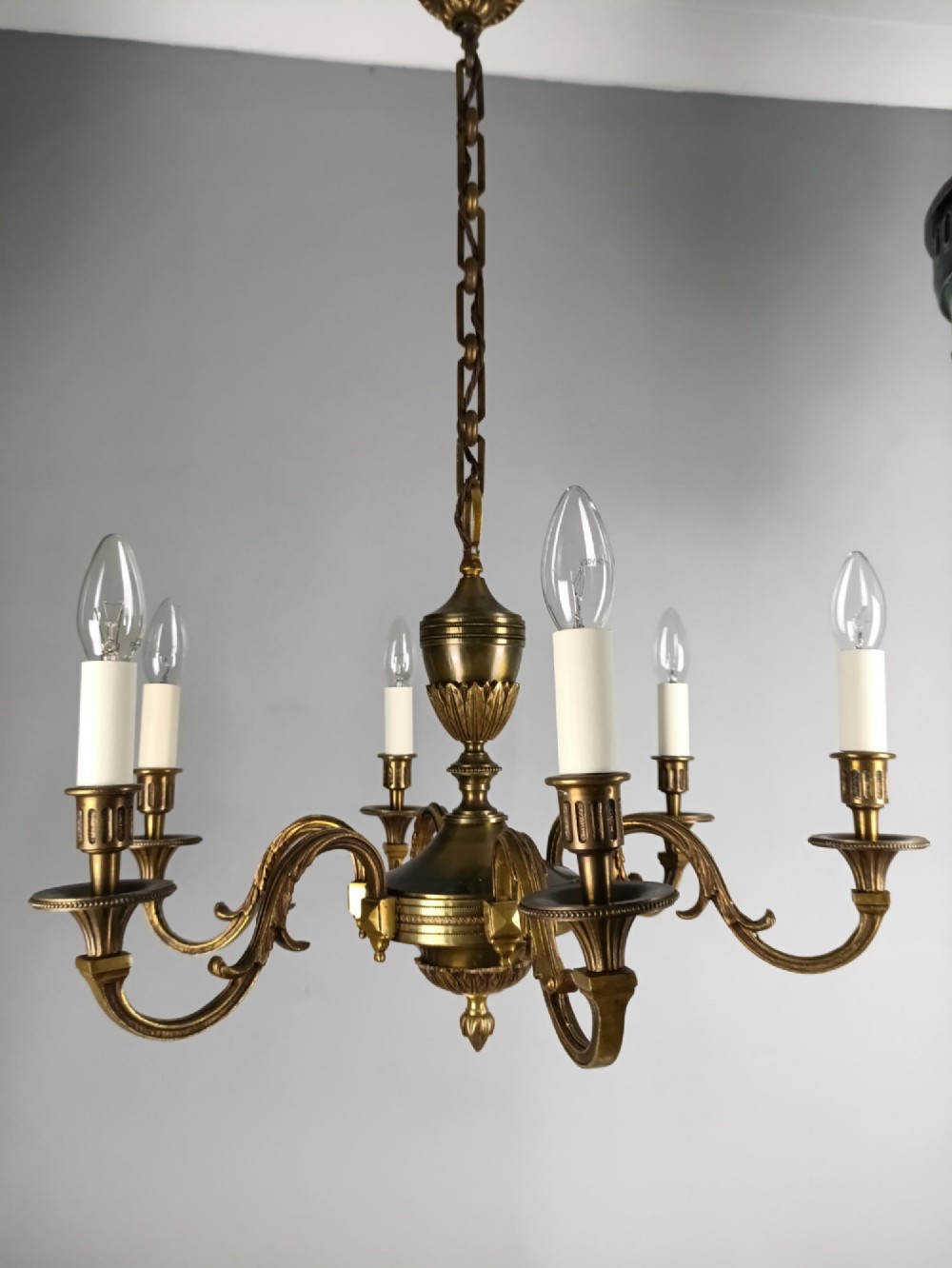 A French antique-style bronze six-arm chandelier featuring scrolling candle arms, white candle sleeves, and a central urn-shaped stem suspended from a metal chain. View VII