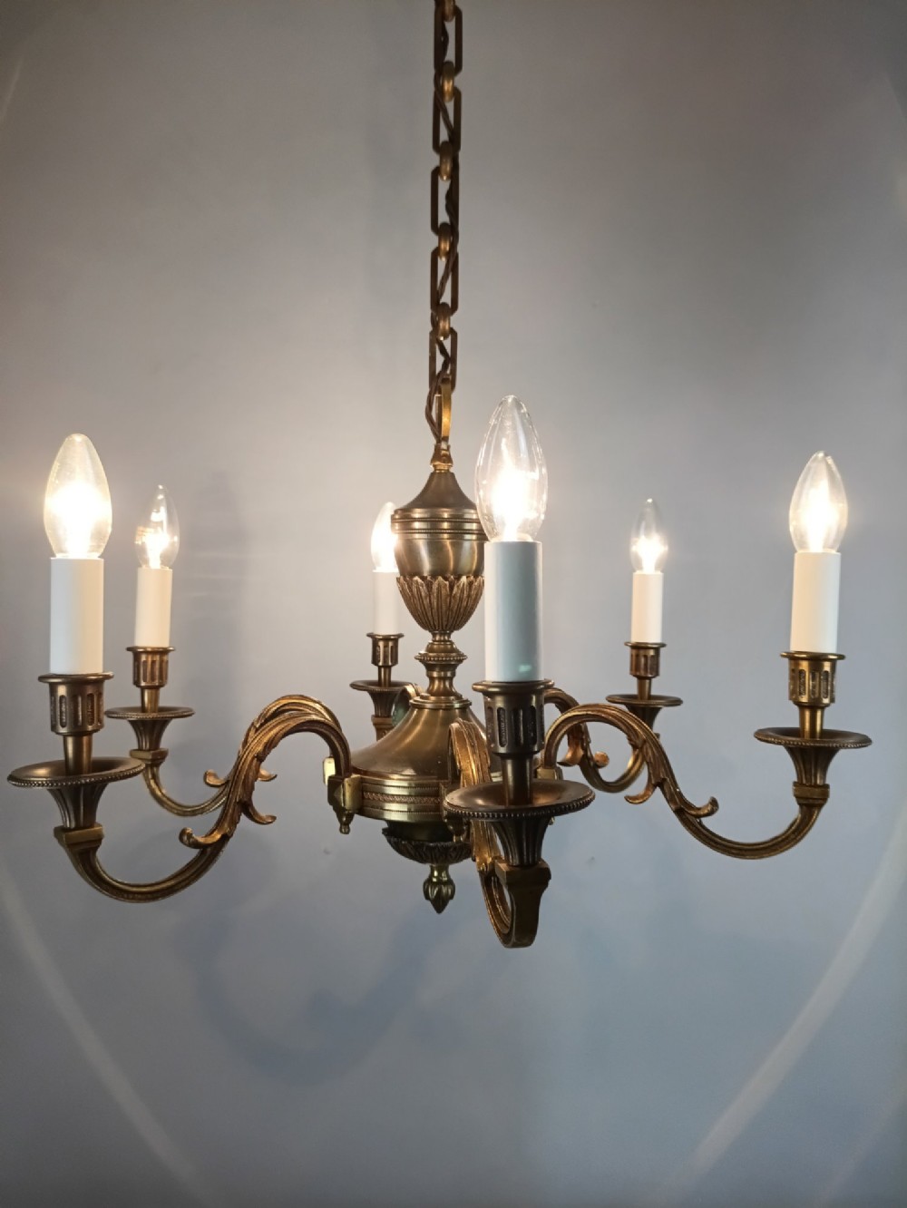 A French antique-style bronze six-arm chandelier featuring scrolling candle arms, white candle sleeves, and a central urn-shaped stem suspended from a metal chain. View VIII