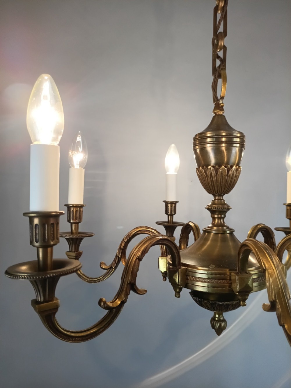 A French antique-style bronze six-arm chandelier featuring scrolling candle arms, white candle sleeves, and a central urn-shaped stem suspended from a metal chain. View IX