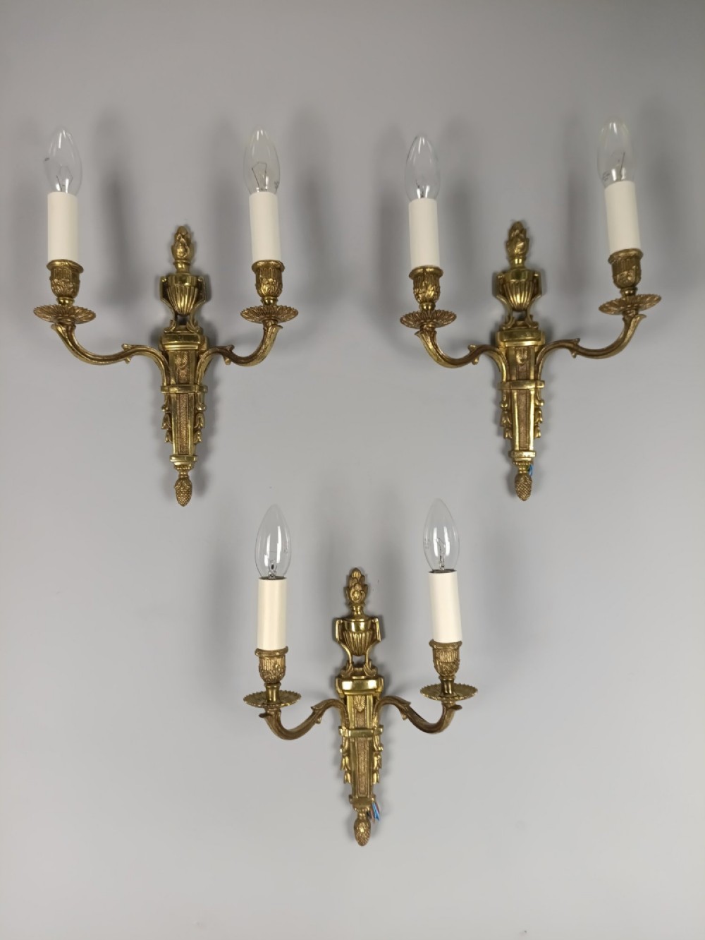 Set of three French Louis XVI style twin-arm wall lights in gilded metal with urn backplates and fluted shafts.