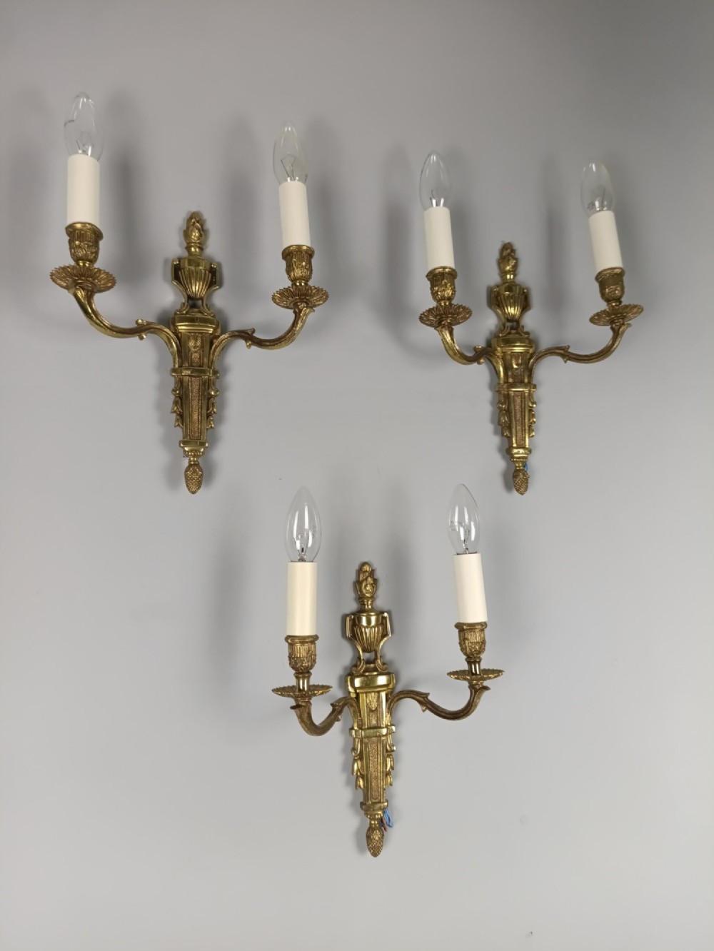 Set of three French Louis XVI style twin-arm wall lights in gilded metal with urn backplates and fluted shafts. View II