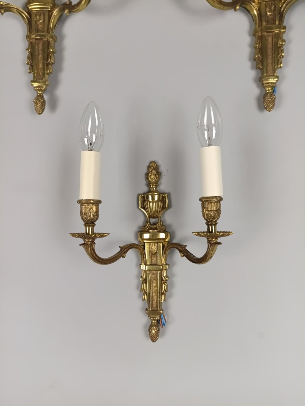 Set of three French Louis XVI style twin-arm wall lights in gilded metal with urn backplates and fluted shafts. View V