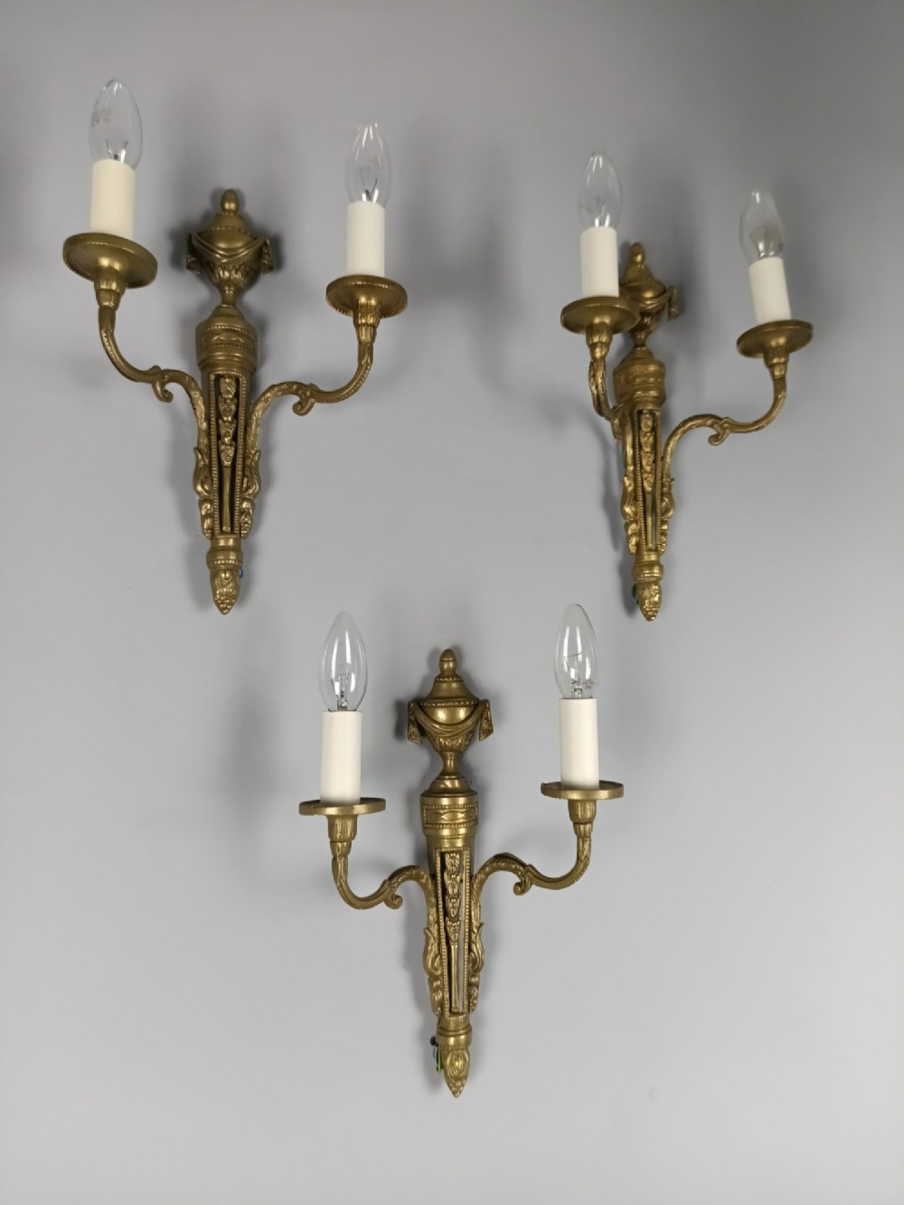A set of three French Neoclassical gilt brass twin-arm wall sconces featuring urn finials and decorative candle branches. View II