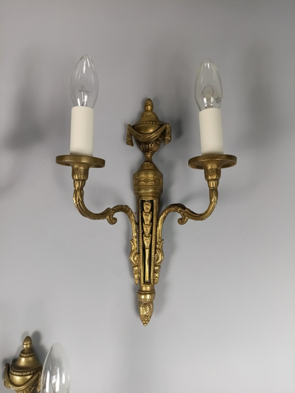 A set of three French Neoclassical gilt brass twin-arm wall sconces featuring urn finials and decorative candle branches. View V