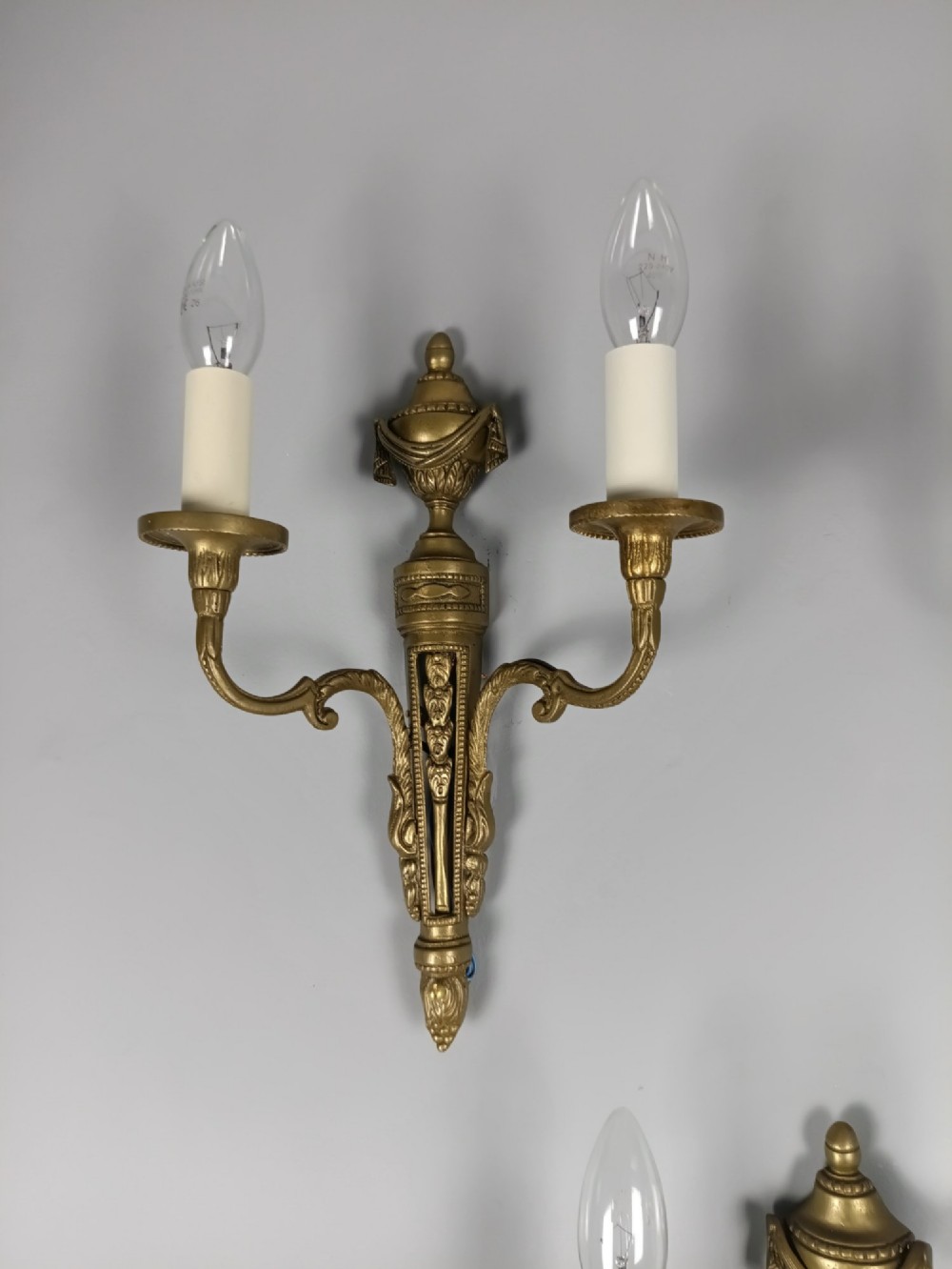 A set of three French Neoclassical gilt brass twin-arm wall sconces featuring urn finials and decorative candle branches. View VI
