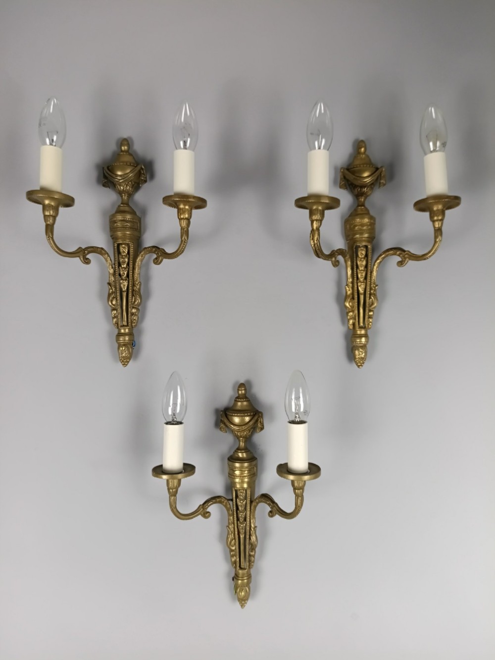 A set of three French Neoclassical gilt brass twin-arm wall sconces featuring urn finials and decorative candle branches. View VII