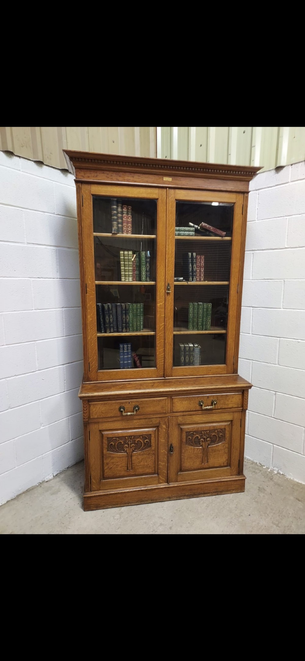 A late 19th-century oak bookcase featuring two glazed upper doors, two waist drawers, and stylised carved relief motifs on the lower cupboard doors.