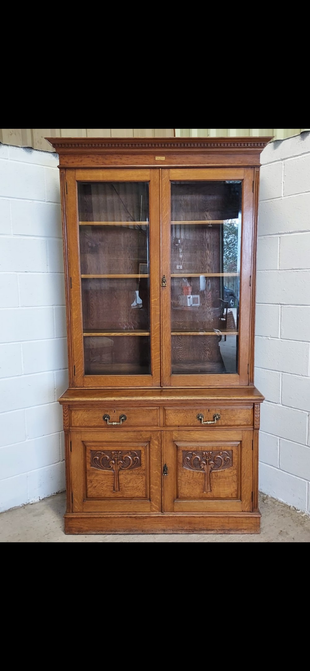 A late 19th-century oak bookcase featuring two glazed upper doors, two waist drawers, and stylised carved relief motifs on the lower cupboard doors. View VI