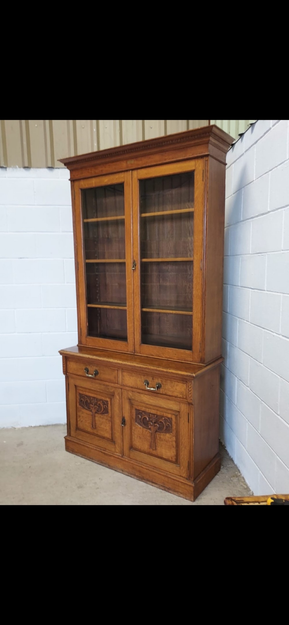 A late 19th-century oak bookcase featuring two glazed upper doors, two waist drawers, and stylised carved relief motifs on the lower cupboard doors. View VII