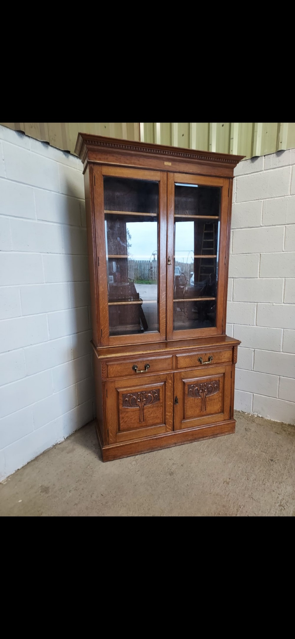 A late 19th-century oak bookcase featuring two glazed upper doors, two waist drawers, and stylised carved relief motifs on the lower cupboard doors. View VIII