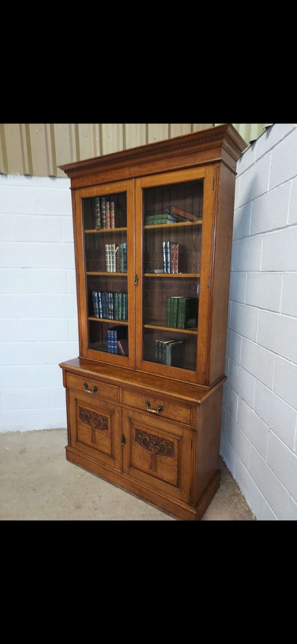 A late 19th-century oak bookcase featuring two glazed upper doors, two waist drawers, and stylised carved relief motifs on the lower cupboard doors. View IX