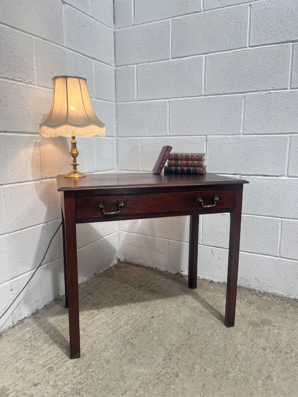 An early nineteenth-century dark oak side table featuring a single frieze drawer with brass drop handles and straight square legs.