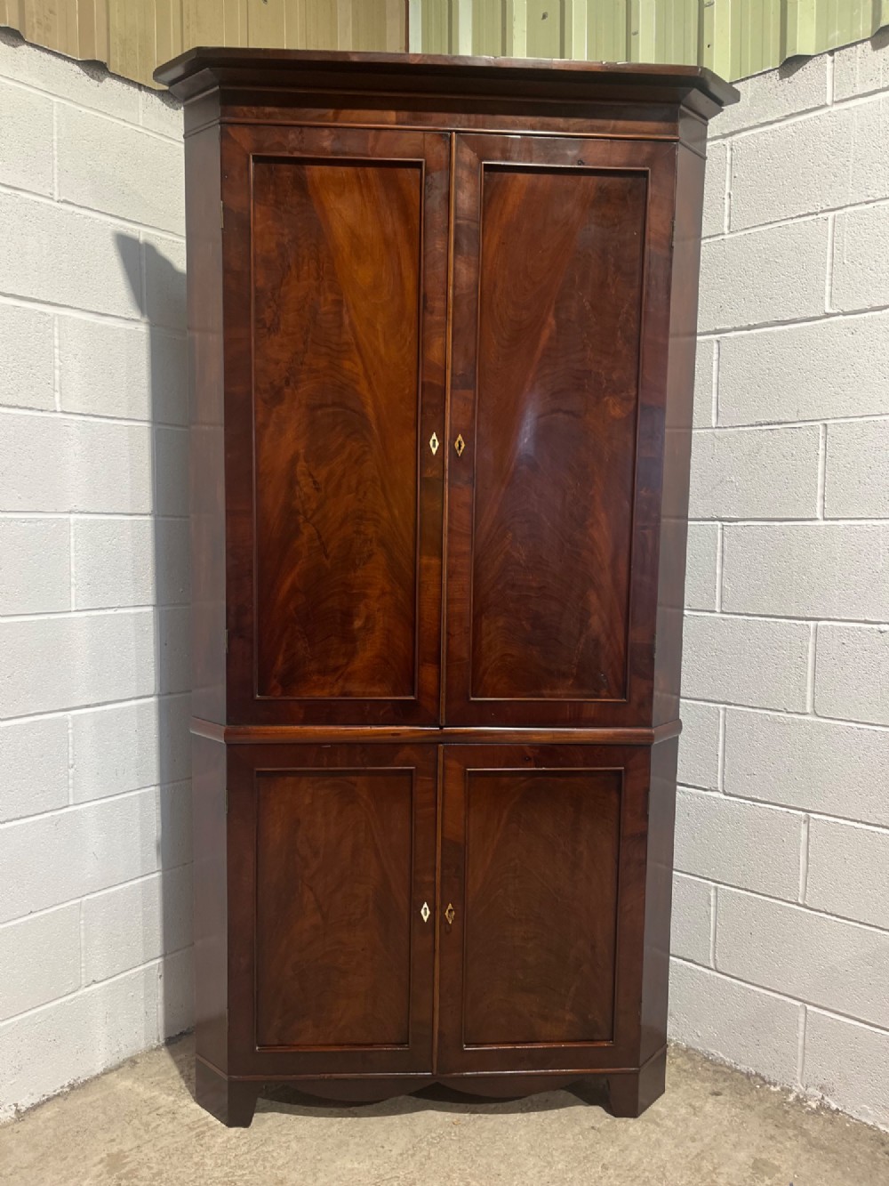A tall Georgian floor-standing corner cupboard crafted from dark flame mahogany with upper and lower double-panelled doors and brass escutcheons. View IV