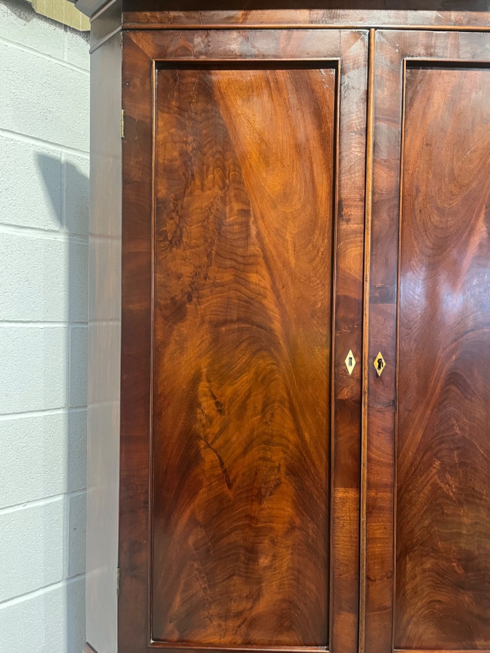 A tall Georgian floor-standing corner cupboard crafted from dark flame mahogany with upper and lower double-panelled doors and brass escutcheons. View VII