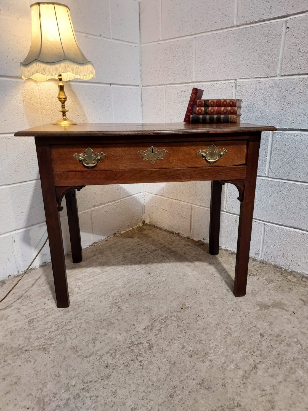 An early 19th-century rectangular oak side table with a single drawer featuring brass handles, a keyhole escutcheon, corner spandrel brackets, and four straight legs. View V