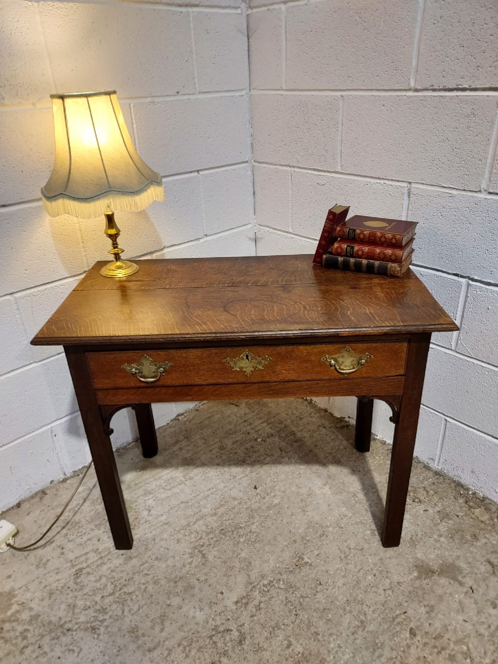 An early 19th-century rectangular oak side table with a single drawer featuring brass handles, a keyhole escutcheon, corner spandrel brackets, and four straight legs. View VI