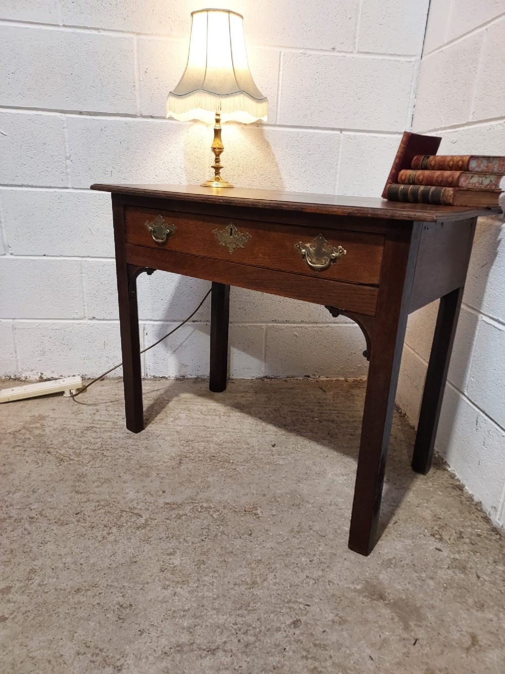 An early 19th-century rectangular oak side table with a single drawer featuring brass handles, a keyhole escutcheon, corner spandrel brackets, and four straight legs. View VIII