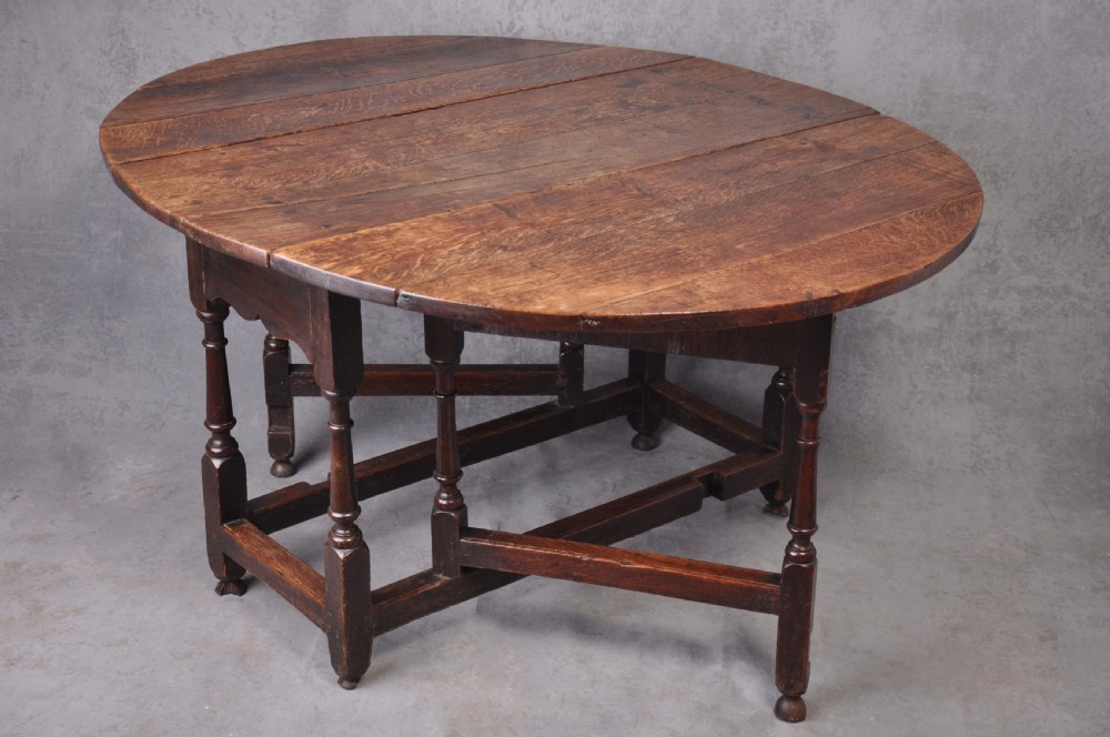 A late seventeenth-century oak gateleg dining table featuring an oval top, turned legs, drop leaves, and a stretcher base.