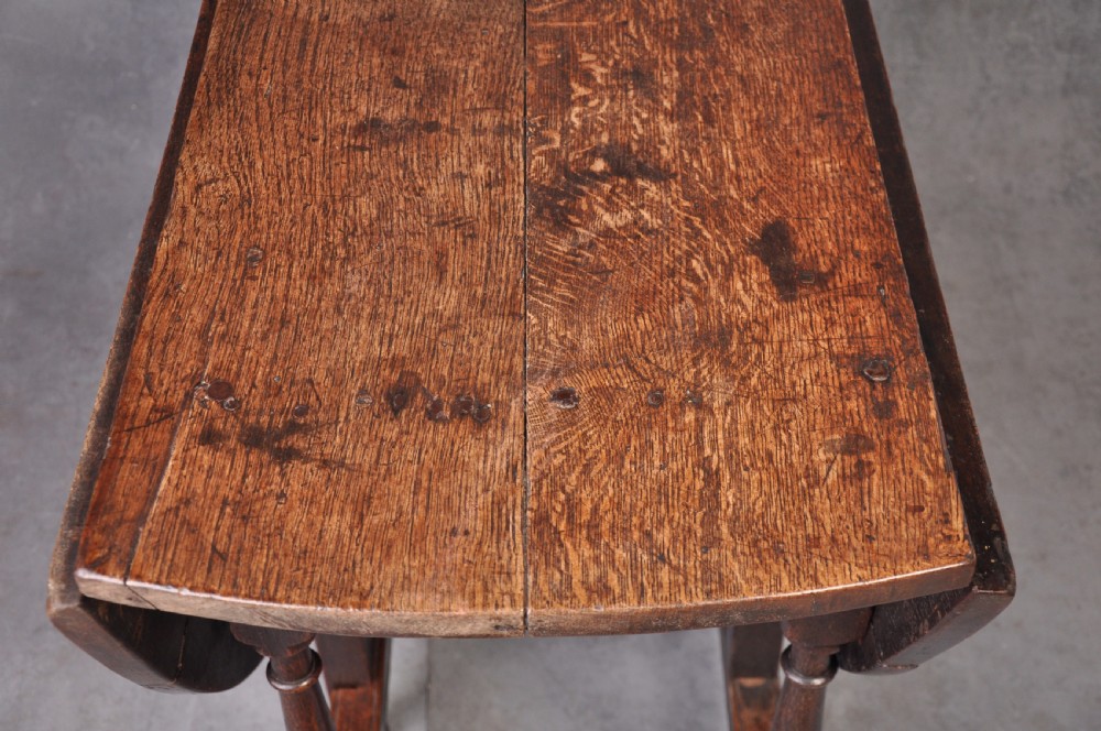 A late seventeenth-century oak gateleg dining table featuring an oval top, turned legs, drop leaves, and a stretcher base. View IV