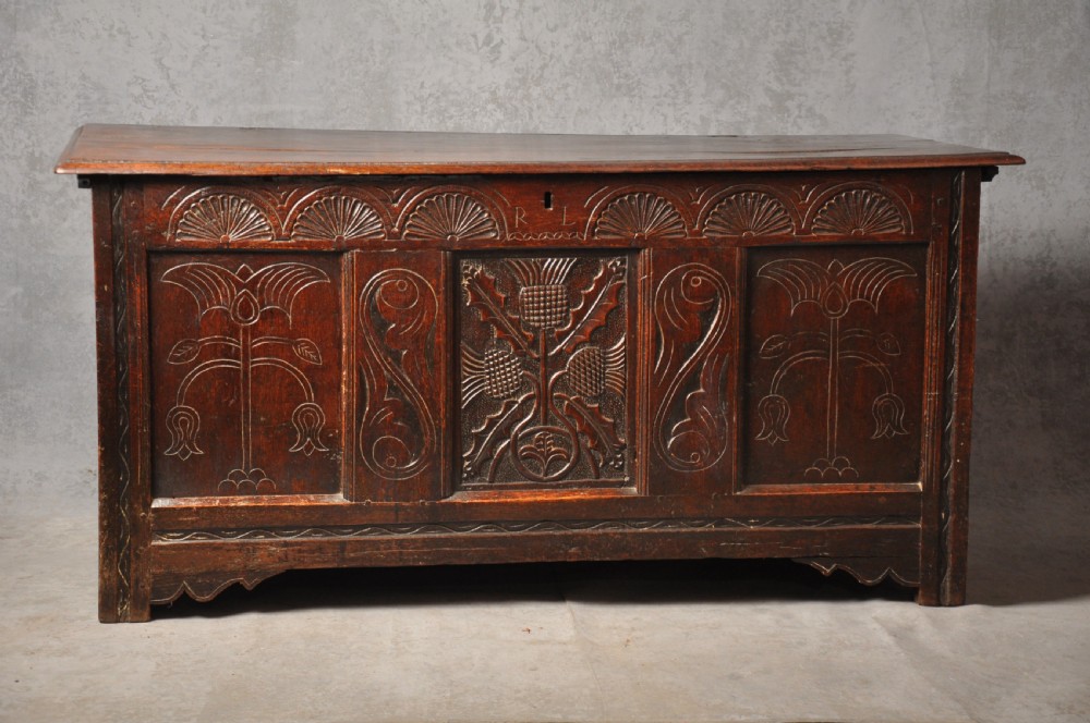 A dark oak 17th-century carved coffer featuring three front panels with a central thistle motif and lunette carvings along the upper rail.