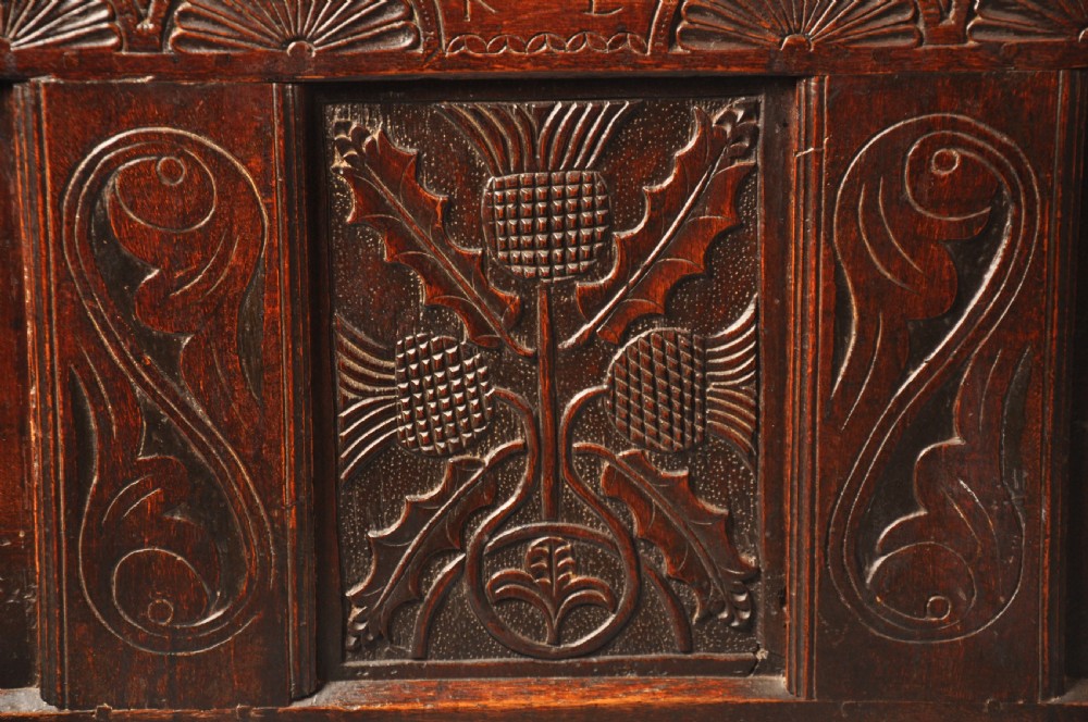 A dark oak 17th-century carved coffer featuring three front panels with a central thistle motif and lunette carvings along the upper rail. View II