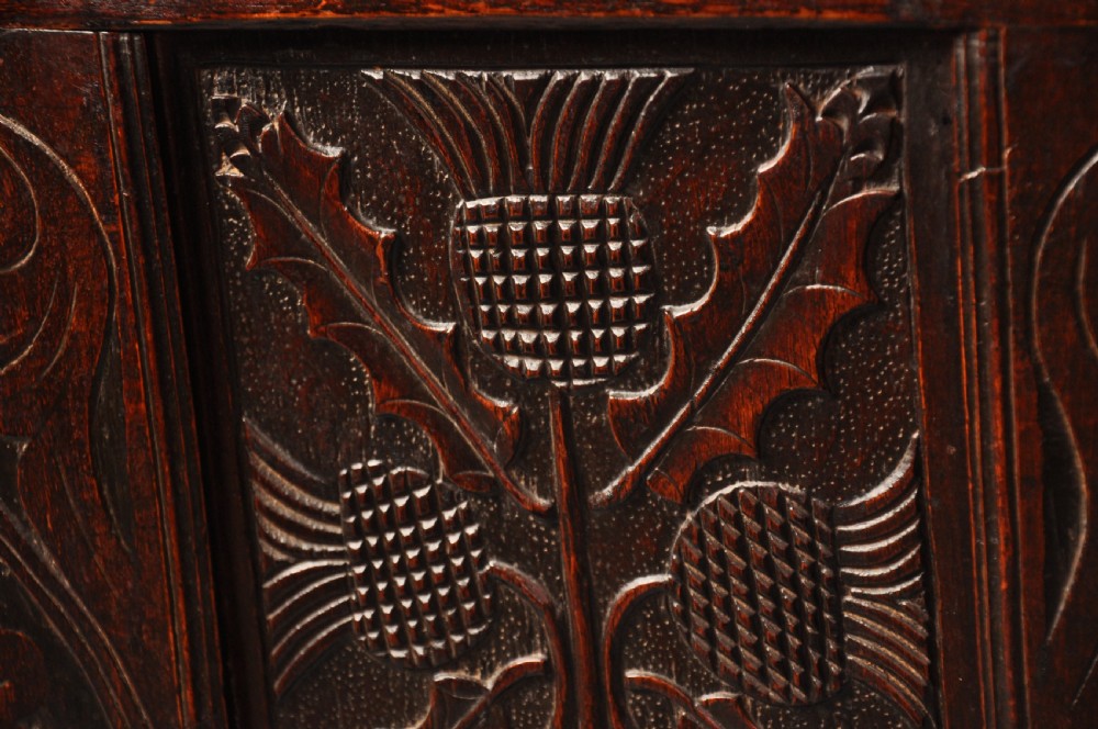 A dark oak 17th-century carved coffer featuring three front panels with a central thistle motif and lunette carvings along the upper rail. View IV
