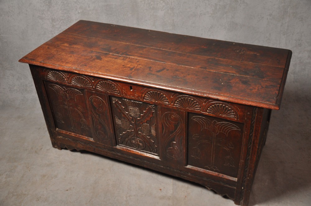 A dark oak 17th-century carved coffer featuring three front panels with a central thistle motif and lunette carvings along the upper rail. View V