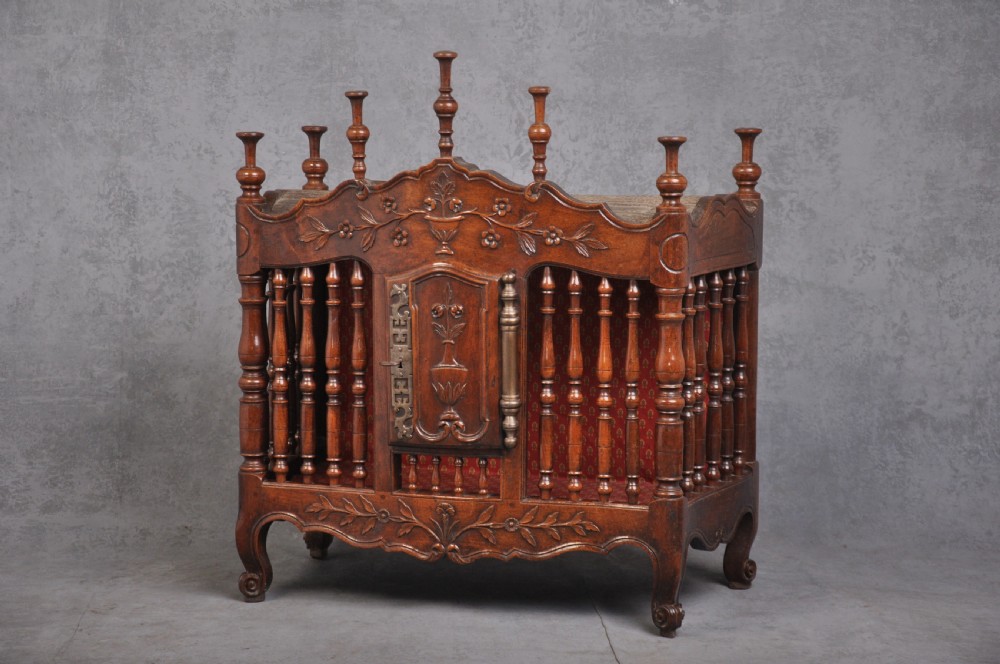 An 18th-century carved walnut French panettiere featuring turned wooden spindles, a central door with carved urn motifs, top finials, and short cabriole legs.