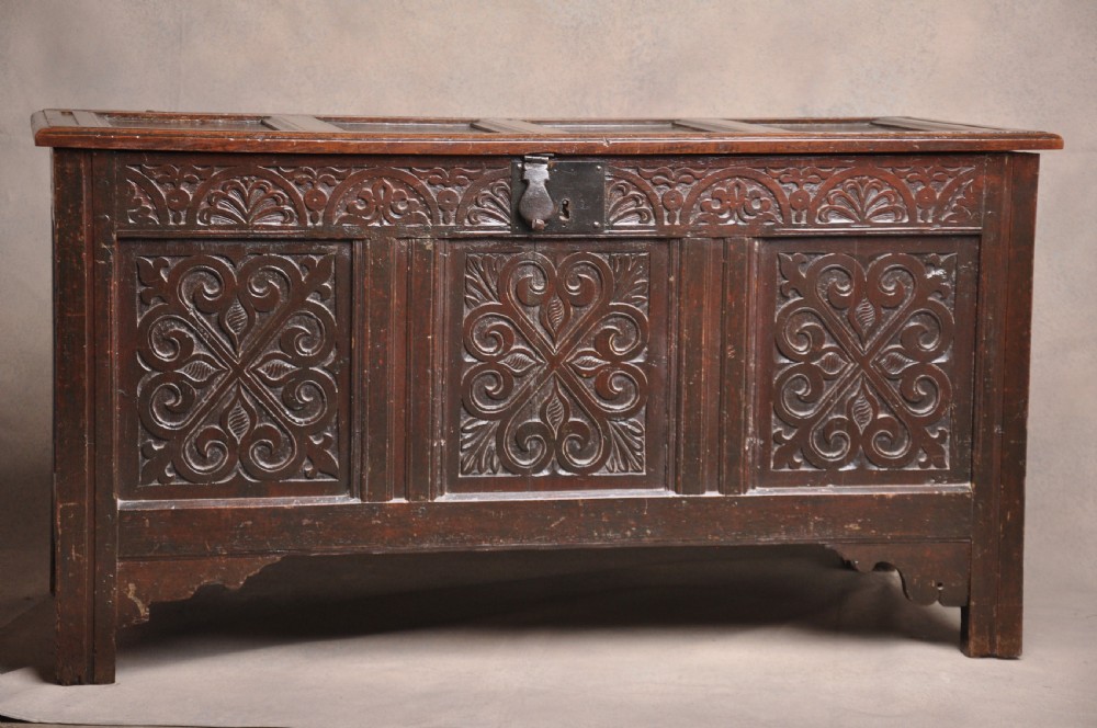 A seventeenth-century dark oak coffer featuring three carved front panels with scrolling leaf motifs, a lunette frieze, and an iron lockplate.