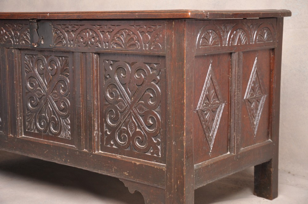 A seventeenth-century dark oak coffer featuring three carved front panels with scrolling leaf motifs, a lunette frieze, and an iron lockplate. View II