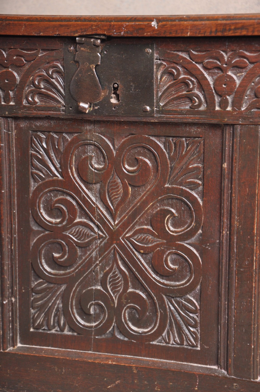 A seventeenth-century dark oak coffer featuring three carved front panels with scrolling leaf motifs, a lunette frieze, and an iron lockplate. View III