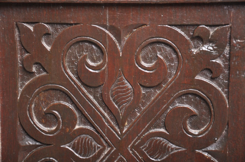 A seventeenth-century dark oak coffer featuring three carved front panels with scrolling leaf motifs, a lunette frieze, and an iron lockplate. View IV