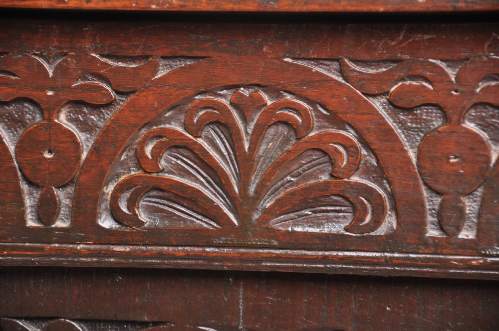 A seventeenth-century dark oak coffer featuring three carved front panels with scrolling leaf motifs, a lunette frieze, and an iron lockplate. View V