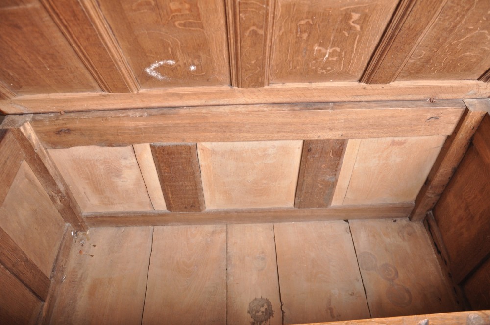 A seventeenth-century dark oak coffer featuring three carved front panels with scrolling leaf motifs, a lunette frieze, and an iron lockplate. View VII