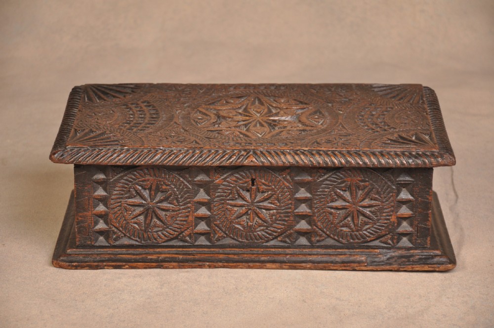A rectangular dark oak box with geometric star chip carvings across the lid and front face, featuring a central iron keyhole.