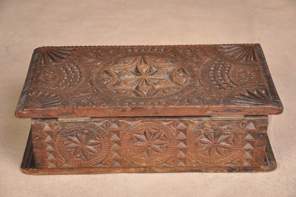A rectangular dark oak box with geometric star chip carvings across the lid and front face, featuring a central iron keyhole. View V