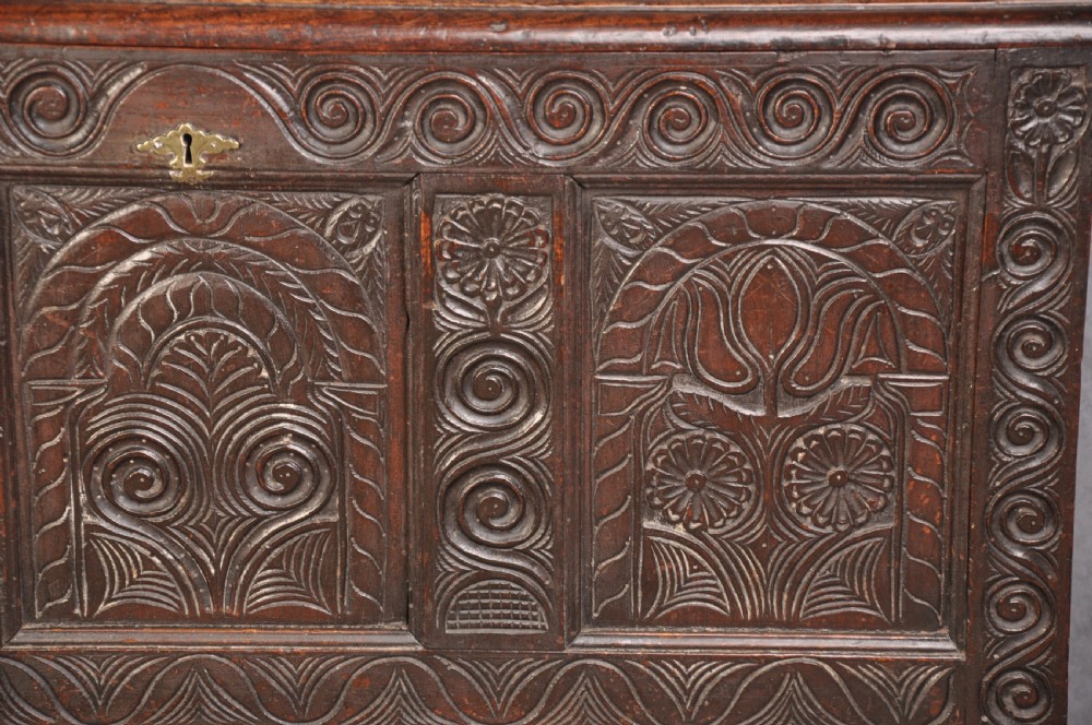 A seventeenth-century carved dark oak Yorkshire coffer featuring three arcaded floral panels, scrollwork friezes, two lower drawers, and brass keyhole escutcheons. View II