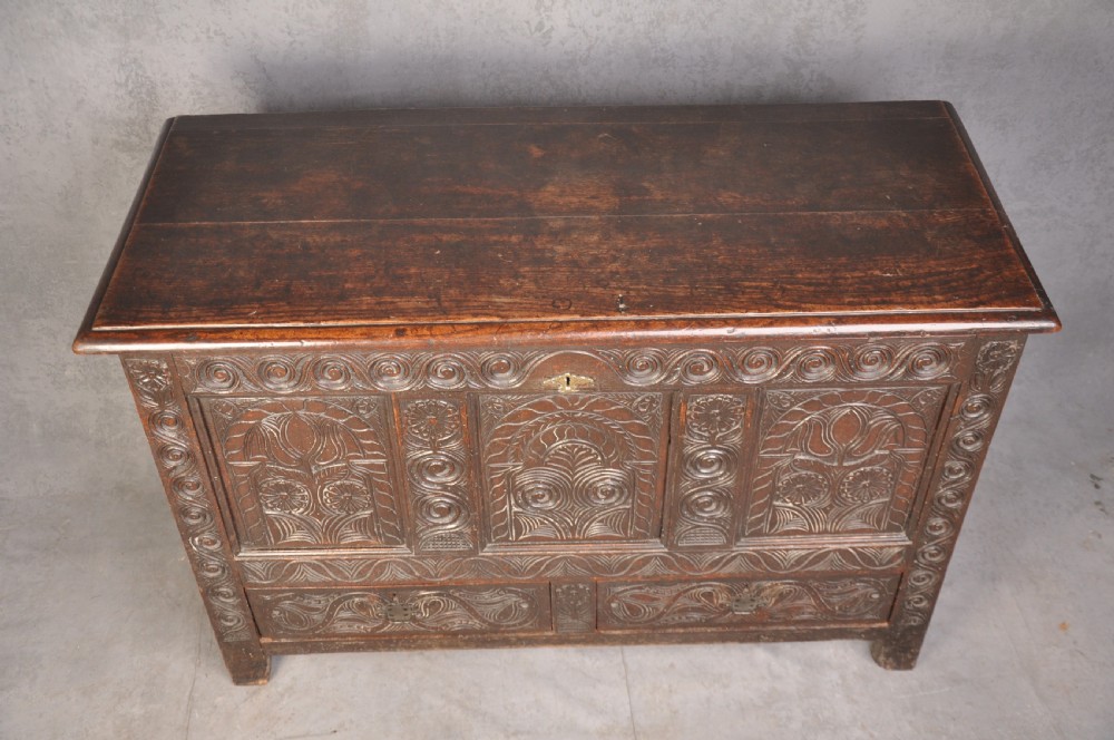 A seventeenth-century carved dark oak Yorkshire coffer featuring three arcaded floral panels, scrollwork friezes, two lower drawers, and brass keyhole escutcheons. View VI