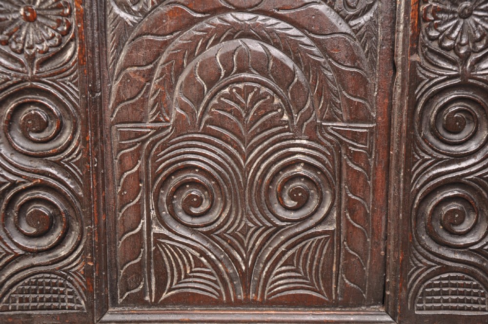 A seventeenth-century carved dark oak Yorkshire coffer featuring three arcaded floral panels, scrollwork friezes, two lower drawers, and brass keyhole escutcheons. View X