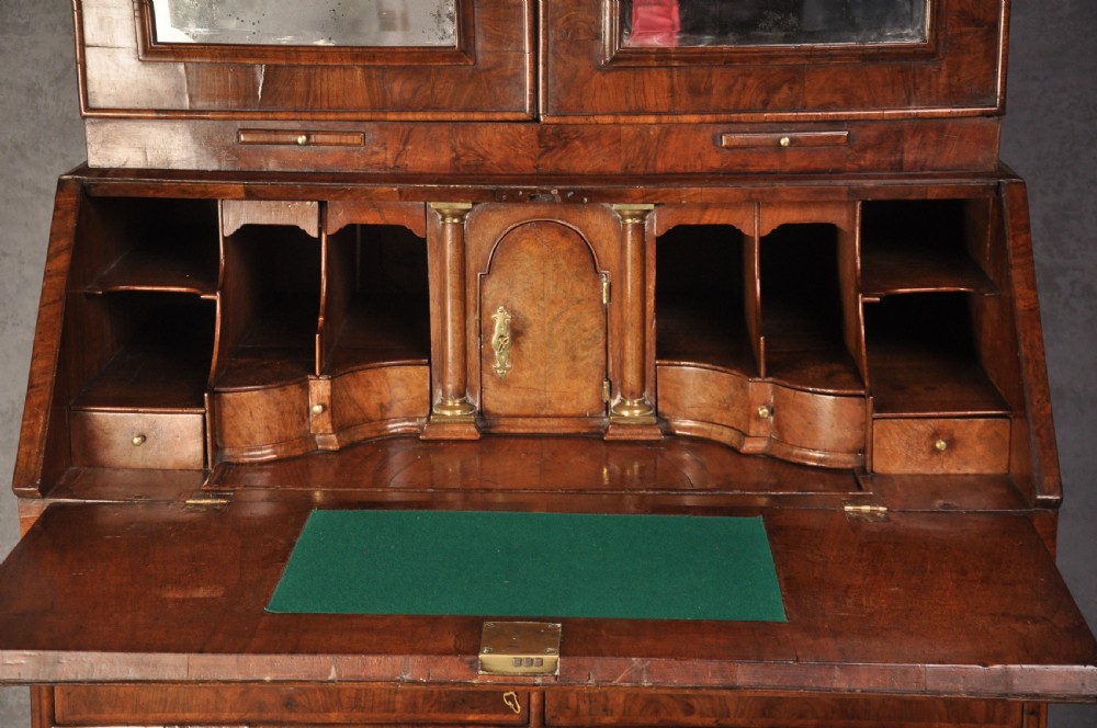 An early 18th-century walnut bureau bookcase with a double-domed top, turned finials, two arched mirrored doors, a slant-front writing slope, and drawers on bracket feet. View III