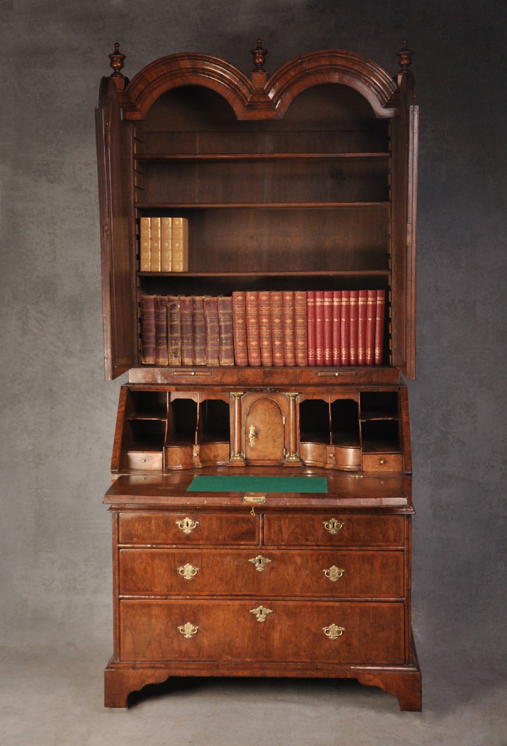 An early 18th-century walnut bureau bookcase with a double-domed top, turned finials, two arched mirrored doors, a slant-front writing slope, and drawers on bracket feet. View IV