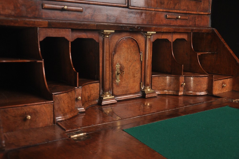 An early 18th-century walnut bureau bookcase with a double-domed top, turned finials, two arched mirrored doors, a slant-front writing slope, and drawers on bracket feet. View V