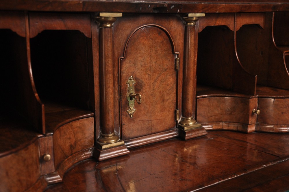 An early 18th-century walnut bureau bookcase with a double-domed top, turned finials, two arched mirrored doors, a slant-front writing slope, and drawers on bracket feet. View VI