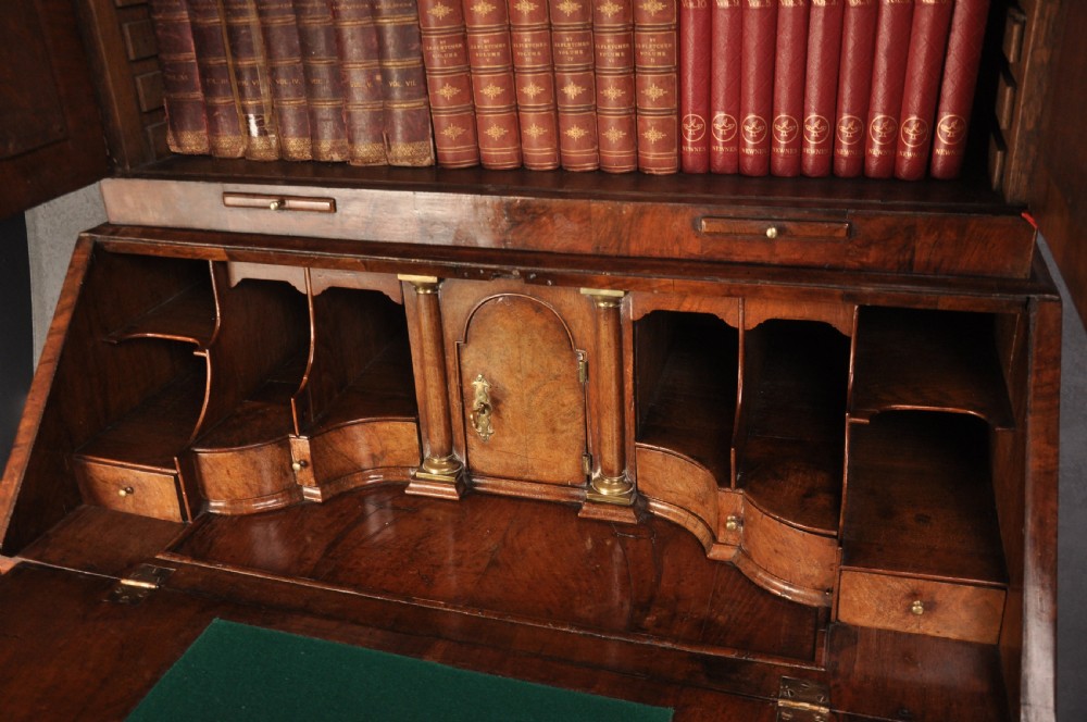 An early 18th-century walnut bureau bookcase with a double-domed top, turned finials, two arched mirrored doors, a slant-front writing slope, and drawers on bracket feet. View VII