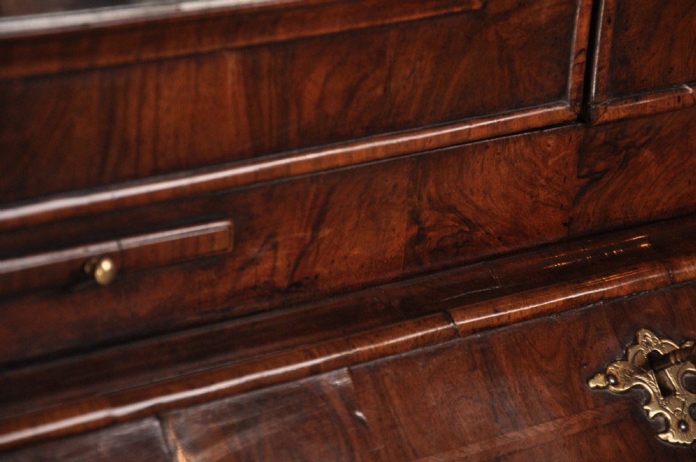 An early 18th-century walnut bureau bookcase with a double-domed top, turned finials, two arched mirrored doors, a slant-front writing slope, and drawers on bracket feet. View XI