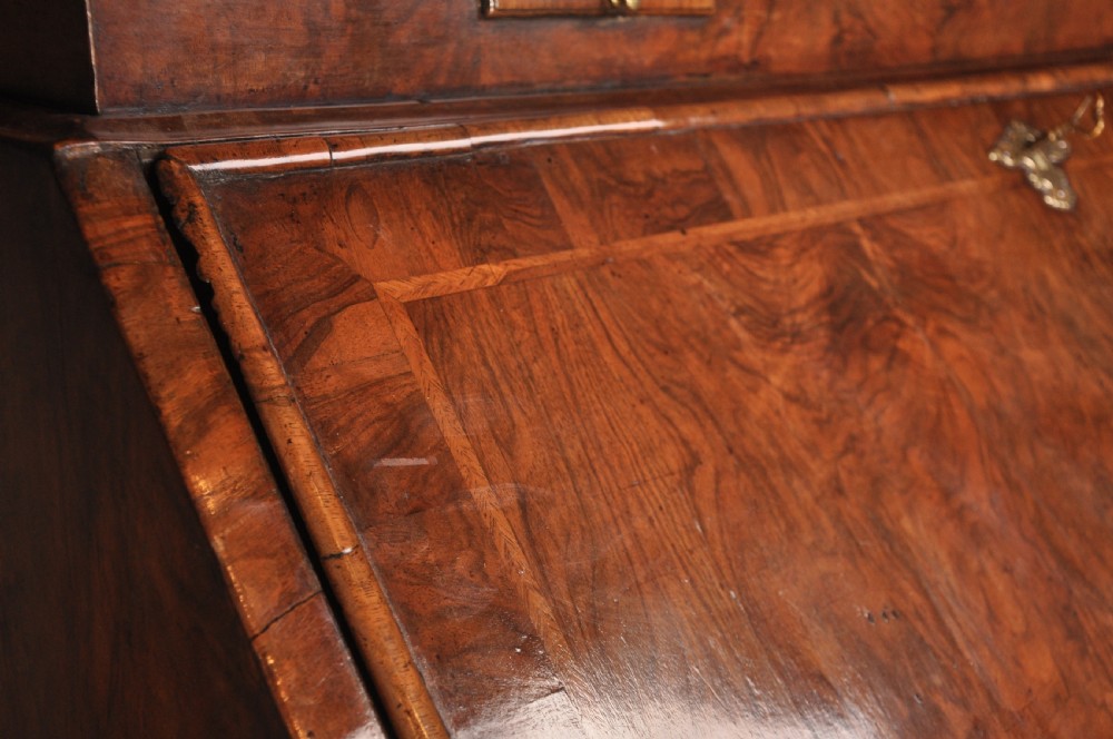 An early 18th-century walnut bureau bookcase with a double-domed top, turned finials, two arched mirrored doors, a slant-front writing slope, and drawers on bracket feet. View XII